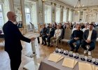 Regierungspräsident Walter Jonas spricht am Rednerpult zu den anwesenden Geehrten, vor ihm liegen Urkunden und Medaillen.