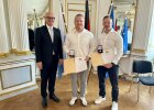 Regierungspräsident Walter Jonas steht neben Christian von der Heiden und Lukas Reil, die Urkunden und Medaillen für ihre Rettung eines LKW-Fahrers entgegennehmen.