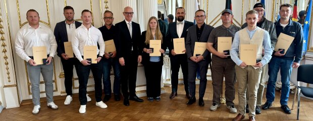 Regierungspräsident Walter Jonas mit den elf Oberpfälzerinnen und Oberpfälzern, die für ihren mutigen Einsatz mit der Öffentlichen Anerkennungsurkunde und Medaille ausgezeichnet wurden. Gruppenfoto mit Regierungspräsident Walter Jonas und den elf Geehrten der Lebensretter-Ehrung in der Regierung der Oberpfalz, alle halten ihre Urkunden in den Händen.